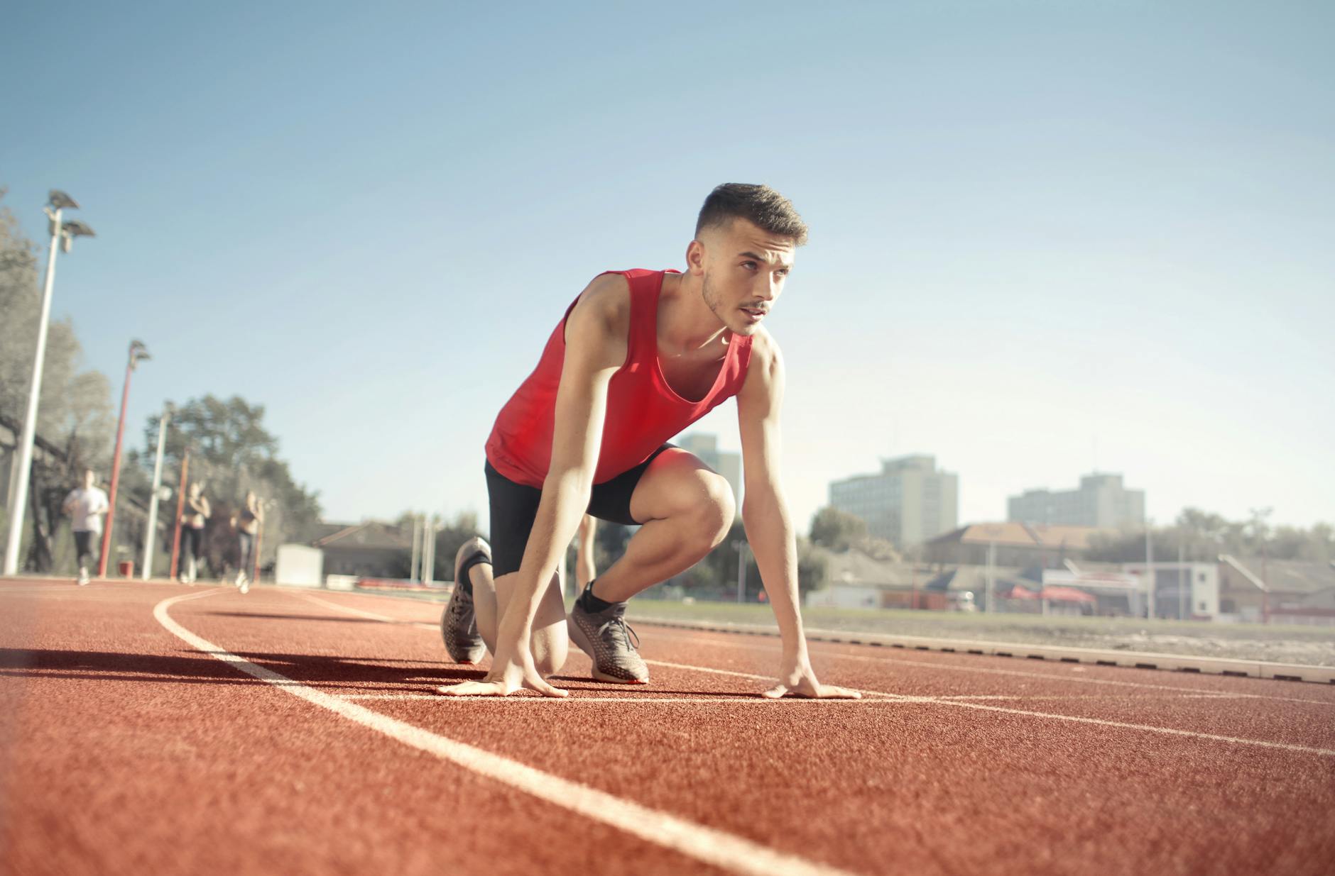 man in res tank top running on athletic field